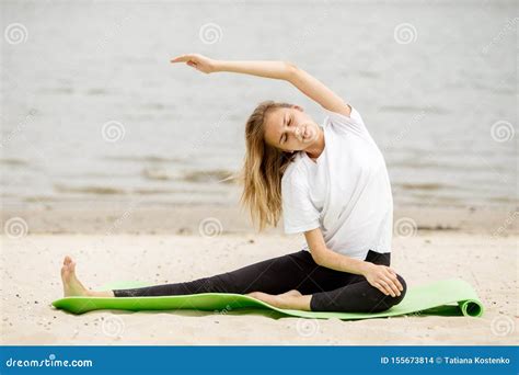 Young Girl Is Doing Stretching On Yoga Mat On Sandy Beach On A Warm Day Zdjęcie Stock Obraz