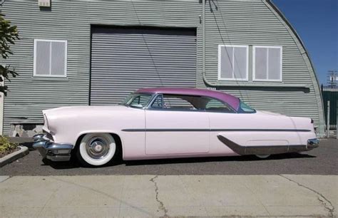 An Old Pink Car Parked In Front Of A Garage