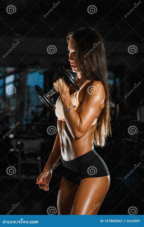 La Donna Atletica Che Pompa Su Muscles Con Le Teste Di Legno Sul Fondo