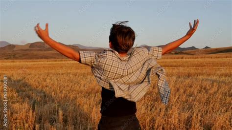 A Teenage Boy Standing In A Mowed Wheat Field At Sunset Raised His