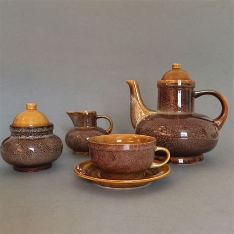 An Assortment Of Teapots And Saucers On A Gray Tableclothed Surface