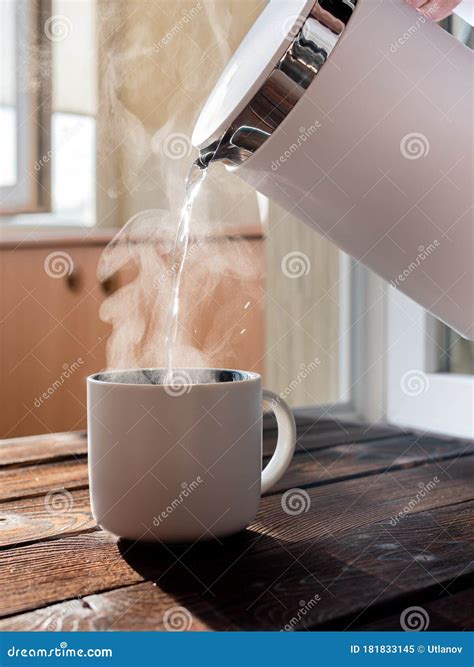 Woman Pouring Boiling Water From The Kettle Into White Cup Standing On