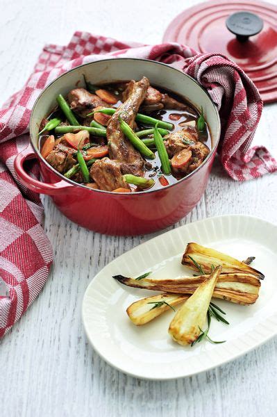 A Red Pot Filled With Meat And Vegetables Next To A White Plate On A Table