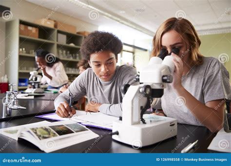 High School Students Looking Through Microscope In Biology Class Stock