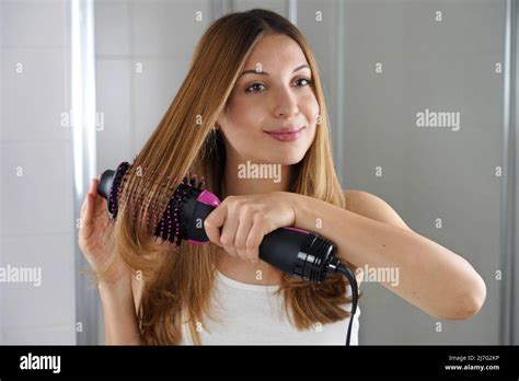 Young Woman Holds Round Brush Hair Dryer To Style Hair In An Easy Way