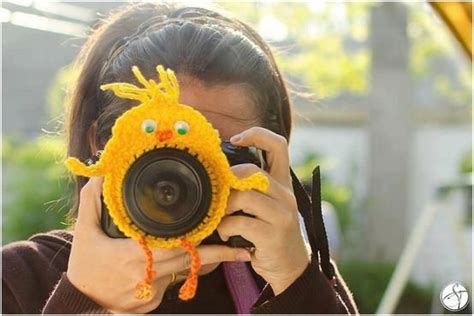 A Woman Holding A Camera Up To Her Face With A Yellow Bird Decoration On It