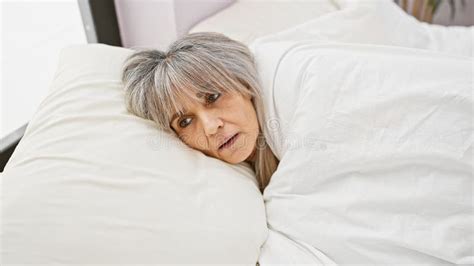 Mature Hispanic Woman With Grey Hair Lying In Bed Portraying Concern Or Contemplation In A Home