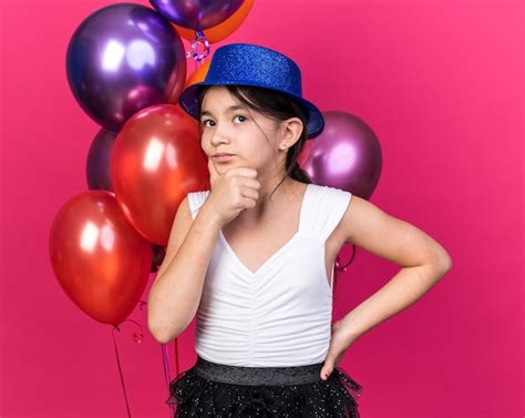 Reflexiva joven caucásica con gorro de fiesta azul sosteniendo la