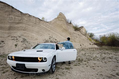 Back of man in jeans jacket and cap is standing, near his white muscle