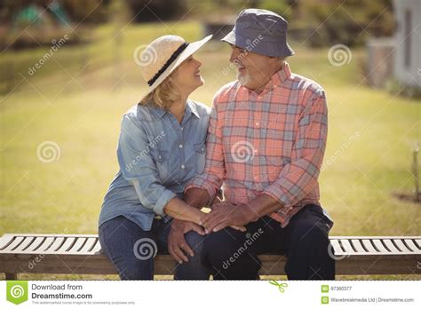 Senior Couple Looking At Each Other While Sitting On A Bench Stock