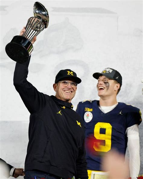 Two Football Players Holding Up Trophies In The Air