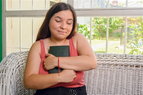 Literatura amorosa jovem latina de olhos fechados sentada em casa abraçando um livro antigo