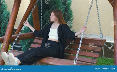 Beautiful Woman Rides On Wooden Swing Pushing Off With Feet Girl Rides On A Swing In Her Yard