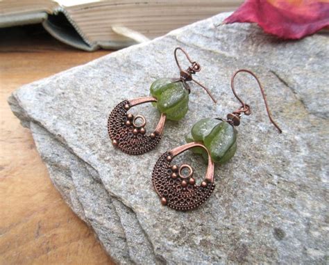 Two Pairs Of Earrings Sitting On Top Of A Rock Next To A Book And Leaf