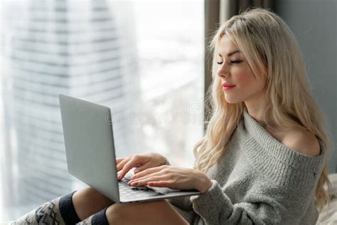 Girl Typing On The Keyboard Beautiful Blonde Woman Sitting On The Bed And Looks At The Laptop