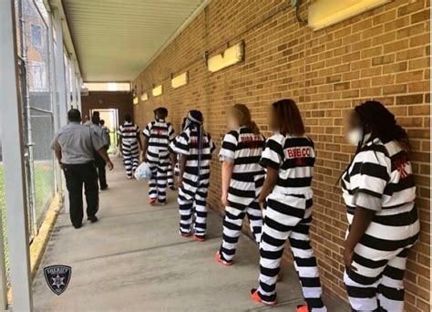 Several People In Jail Uniforms Lined Up Against A Brick Wall With One