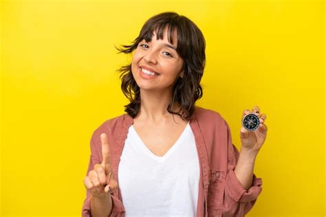 Joven latina sosteniendo una brújula aislada de fondo amarillo