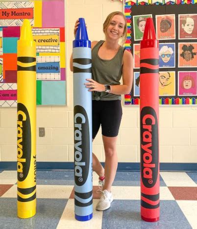 A Woman Standing Next To Two Giant Crayons In The Middle Of A Room