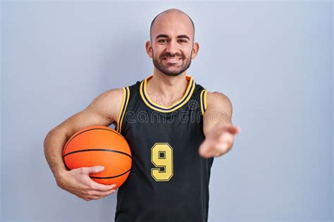 Young Bald Man With Beard Wearing Basketball Uniform Holding Ball