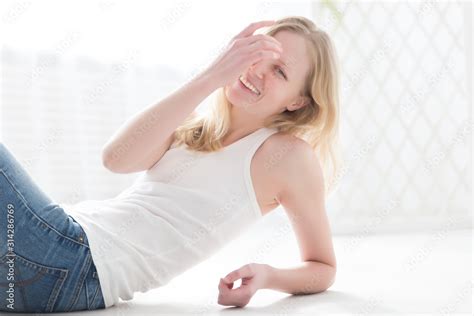 Beautiful Blonde Woman In Jeans And A White T Shirt On The Floor In A Bright Room Stock Photo