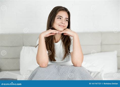 Young Attractive Woman Sitting In Bed In Bright Bedroom Holding Her Hands Near Face In The