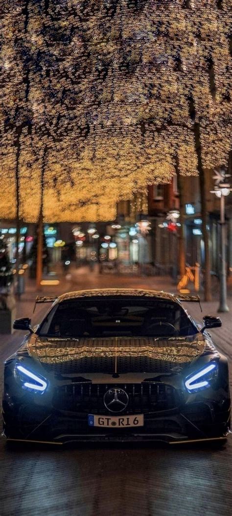 The Front End Of A Car Parked On A Street At Night With Trees In The