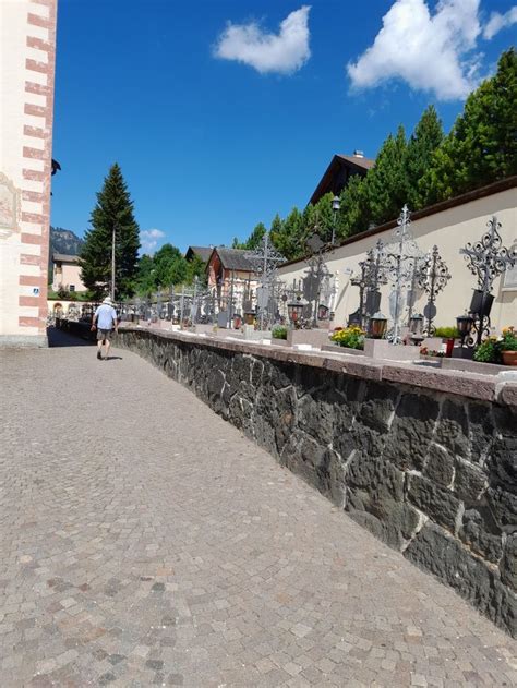 A Man Walking Down A Street Next To A Stone Wall With Statues On The Side