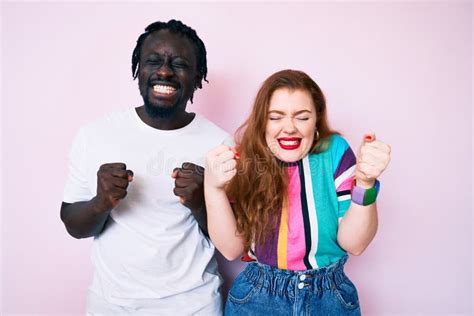 Interracial Couple Wearing Casual Clothes Excited For Success With Arms