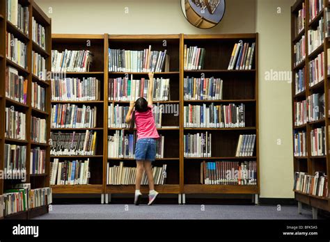 Girl Reaching For Book On Library Shelf Stock Photo Alamy