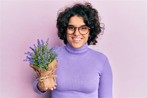 Young Hispanic Woman With Curly Hair Holding Lavender Plant Looking