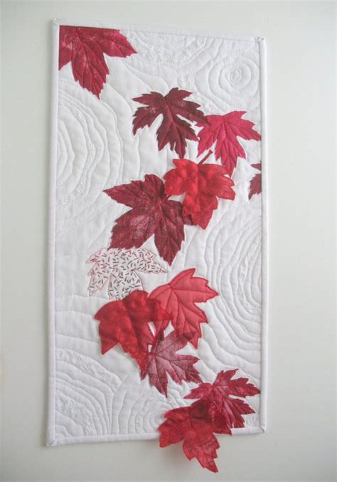 A Quilted Wall Hanging With Red Leaves On It