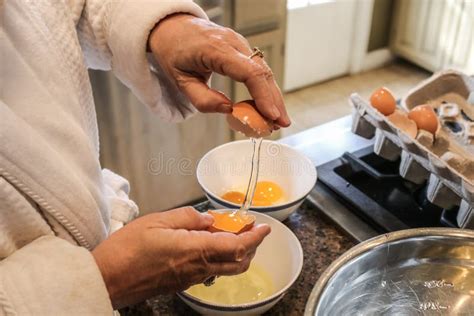 Hands Of Mature Woman In Bathrobe Separating Eggs On Island In Kitchen