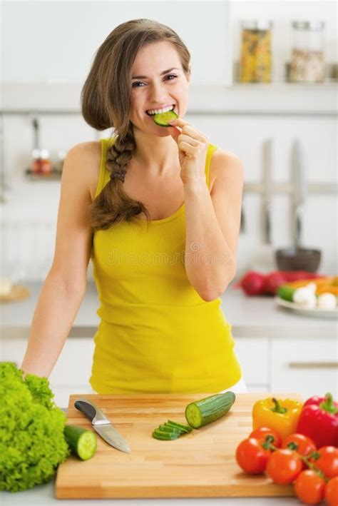 Happy Young Woman Biting Cucumber While Cutting Fresh Salad Stock Image