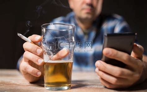 酒精中毒、酒精成瘾和人的观念 男性酗酒者晚上用智能手机喝啤酒和抽烟。高清摄影大图 千库网