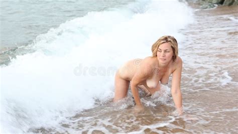 Naked Woman Is Sitting In Rays Of Setting Sun On Seashore In Surf