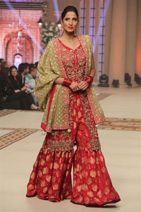 A Woman In A Red And Gold Outfit Walking Down The Runway At A Fashion Show