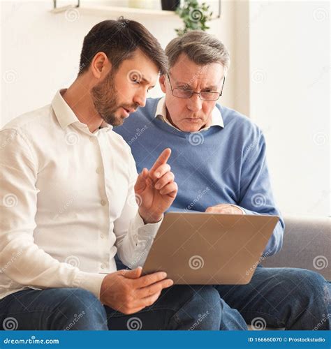 Mature Son Explaining Father How To Use Laptop Sitting Indor Stock