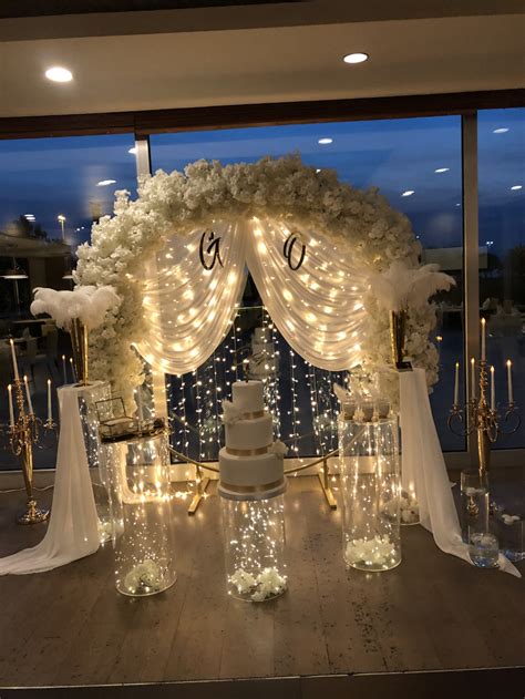 A Wedding Cake Is Displayed In Front Of A Window With Lights And