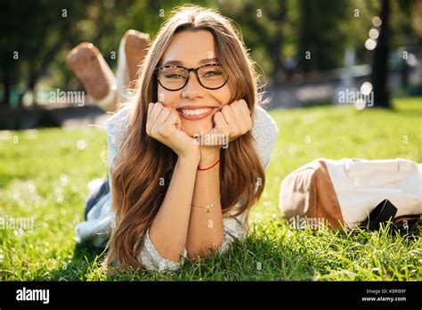 Smiling Brunette Woman In Eyeglasses Lying On Grass In Park While