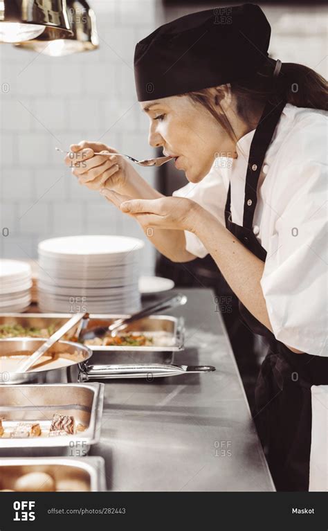 Side view of female chef tasting food at commercial kitchen stock photo ...