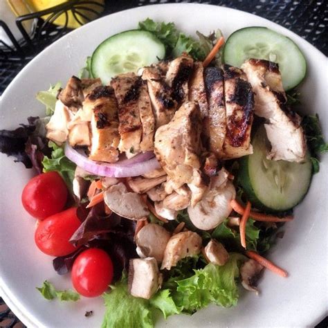 A Salad With Chicken Cucumbers Tomatoes And Lettuce On A White Plate