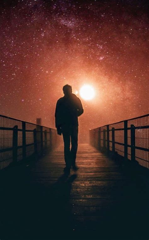 A Man Is Walking Across A Bridge At Night With The Stars In The Sky Above