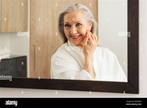 Mature Woman With Long Grey Hair Looking At A Mirror In A Bathroom