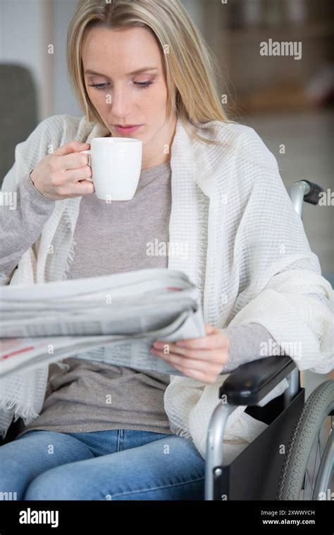 Blonde Woman Having Coffee While Reading Newspaper At Home Stock Photo