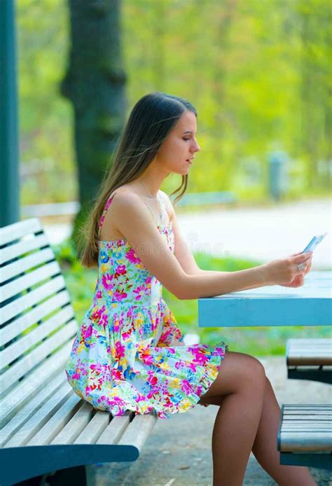 Smiling Woman In Summer Dress Seated Outdoors On Chair Stock Photo