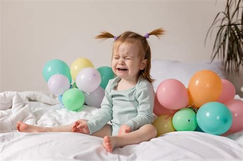 Niña llorando sentada en la cama con globos foto de alta calidad Foto