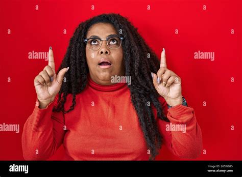 Plus Size Hispanic Woman Standing Over Red Background Amazed And Surprised Looking Up And