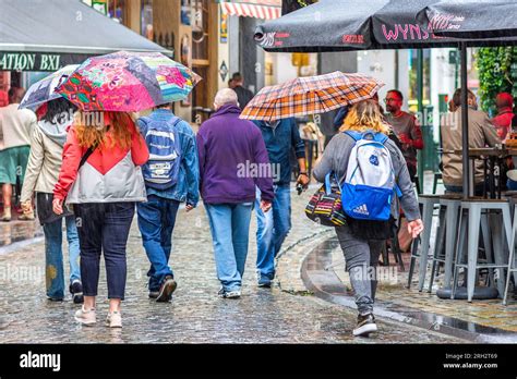 Group Of People Walking Along City Center Street Holding Umbrellas