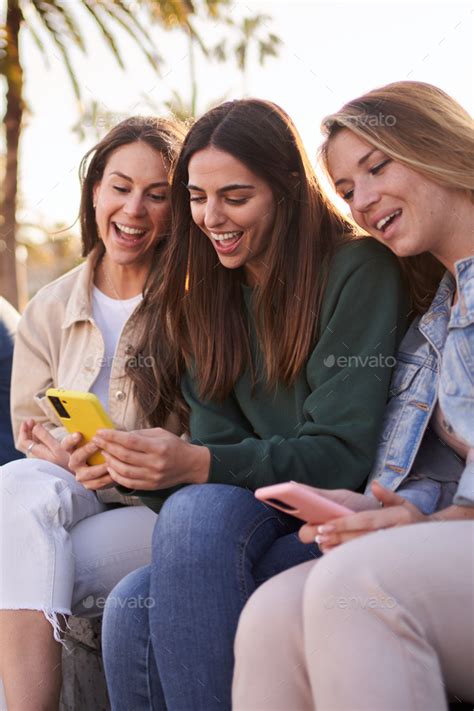 Group Of Gen Z Beautiful Female Friends Smiling Sitting Outdoors Using