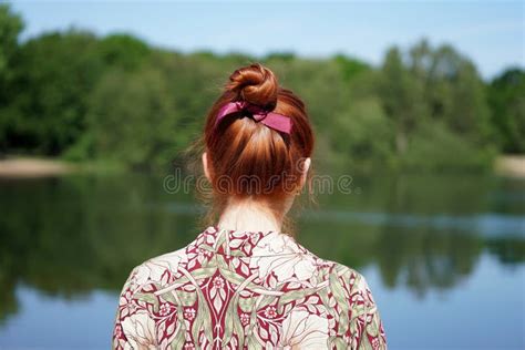 Opini N Trasera La Mujer Con El Bollo Rojo Del Pelo Que Mira El Lago